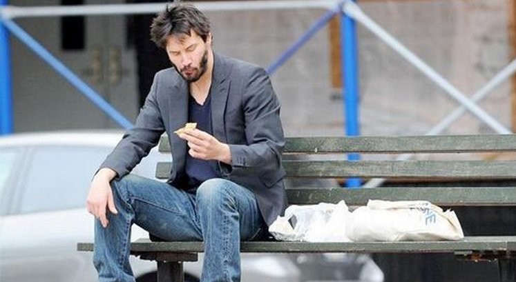 Keanu Reeves enjoys a snack on a bench 