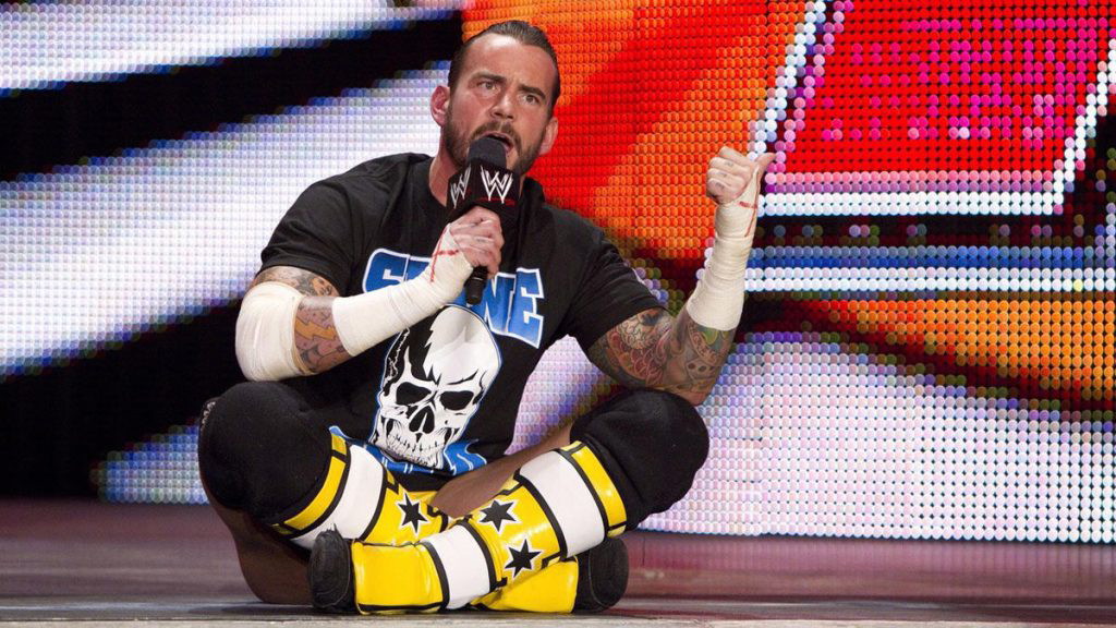 CM Punk sitting on the ground holding a mic during a wrestling event.