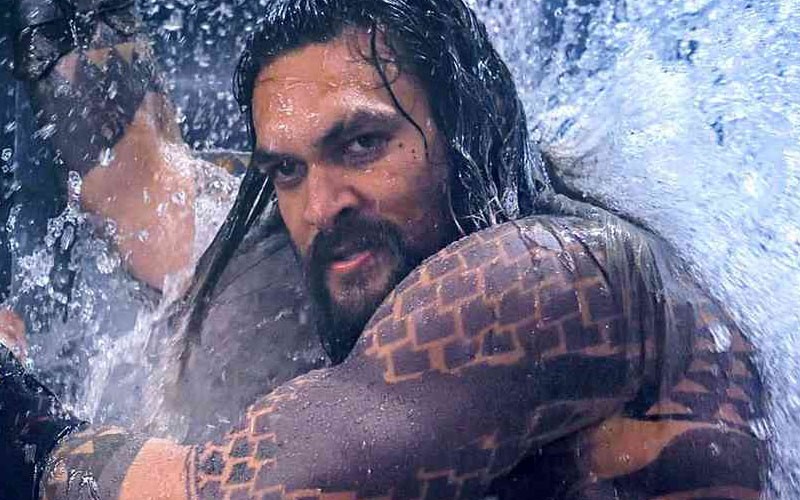 Jason Momoa holding something against a raging body of water in this scene