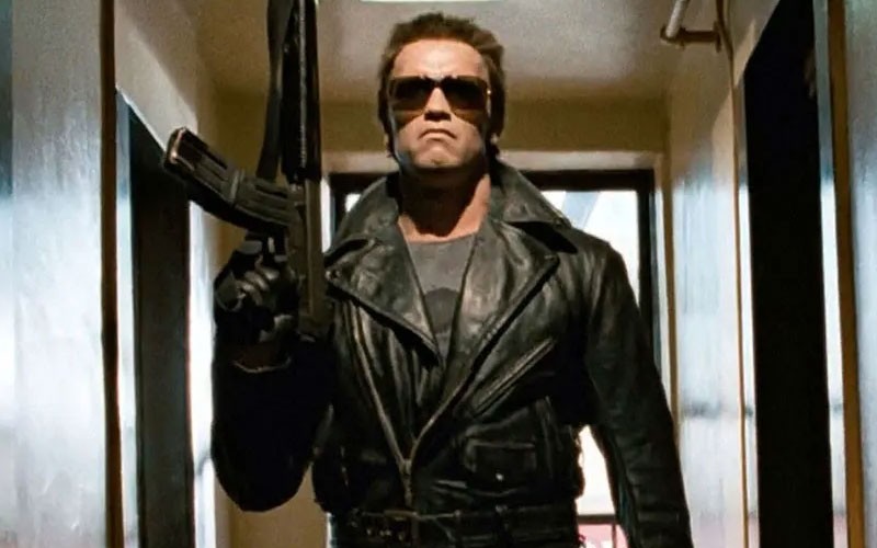Arnold Schwarzenegger as The Terminator while holding a carbine 