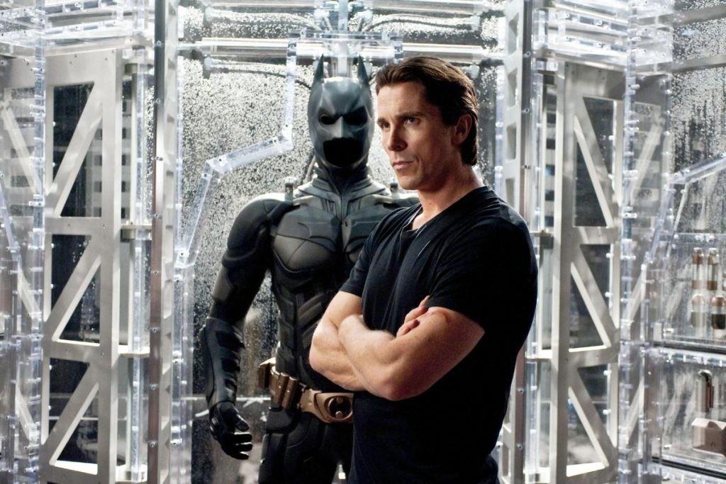 Christian Bale's Batman standing by his Batsuit