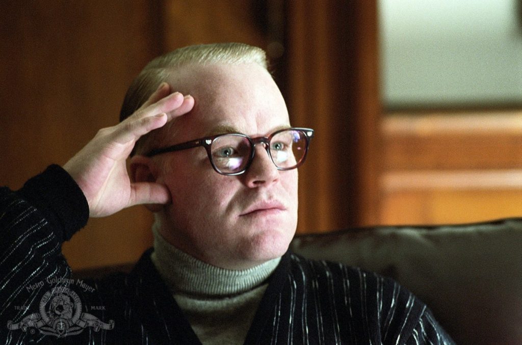 Philip Seymour Hoffman in and as Capote sitting grimly