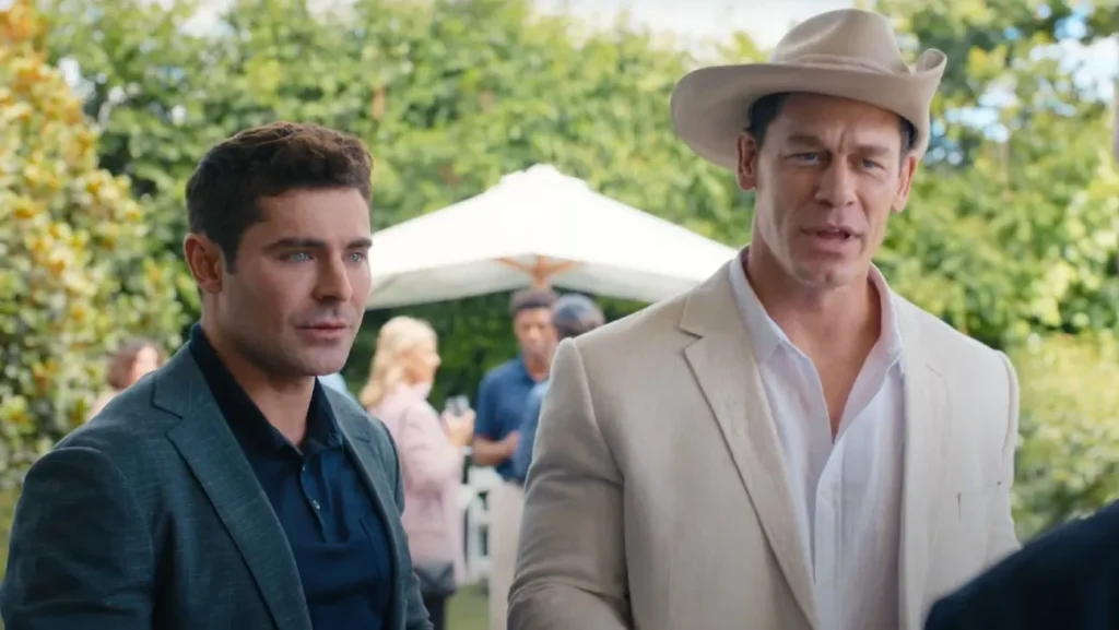 Zac Efron and John Cena in a cowboy hat talking to someone in Ricky Stanicky