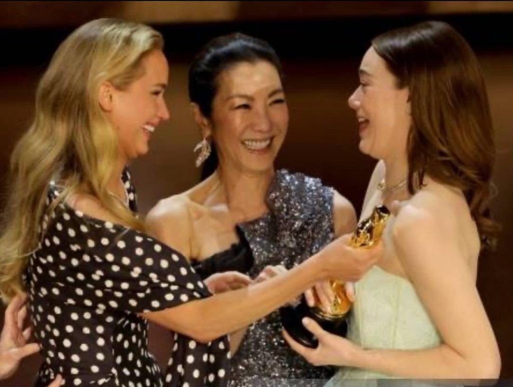 Emma Stone receiving the award from both Michelle Yeoh and Jennifer Lawrence