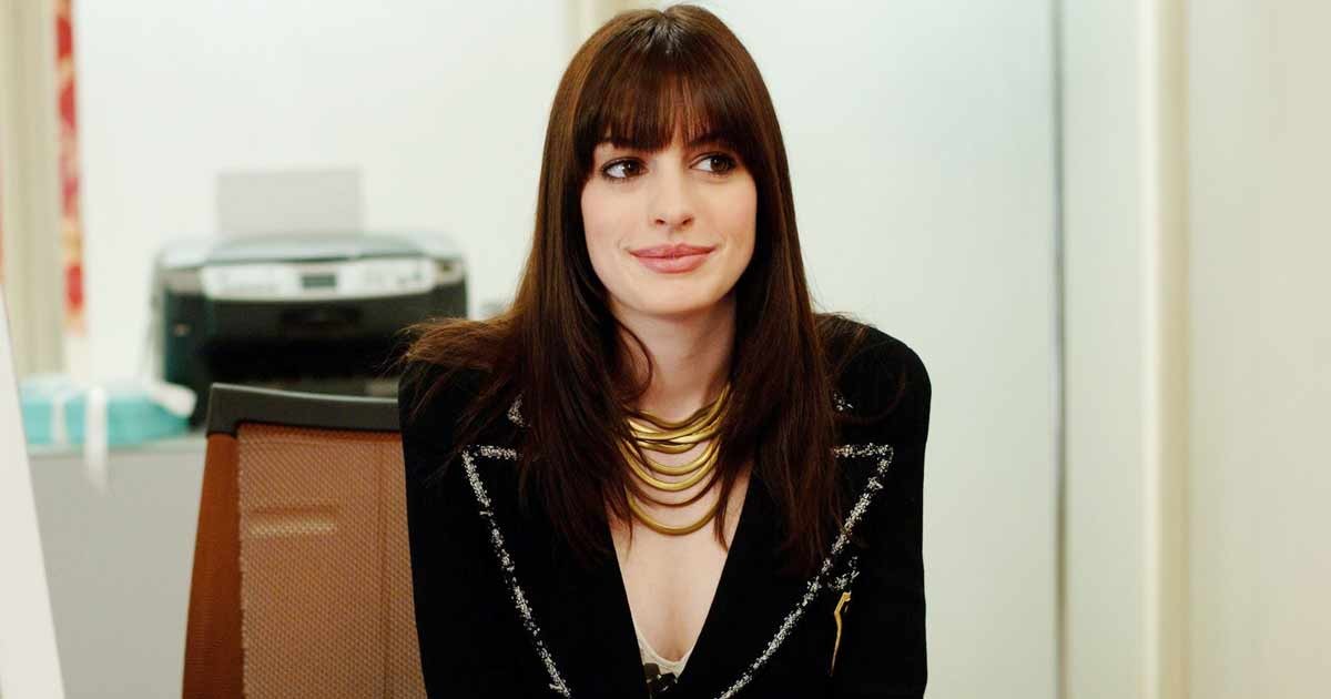 Anne Hathaway sits on the desk of her workplace in The Devil Wears Prada