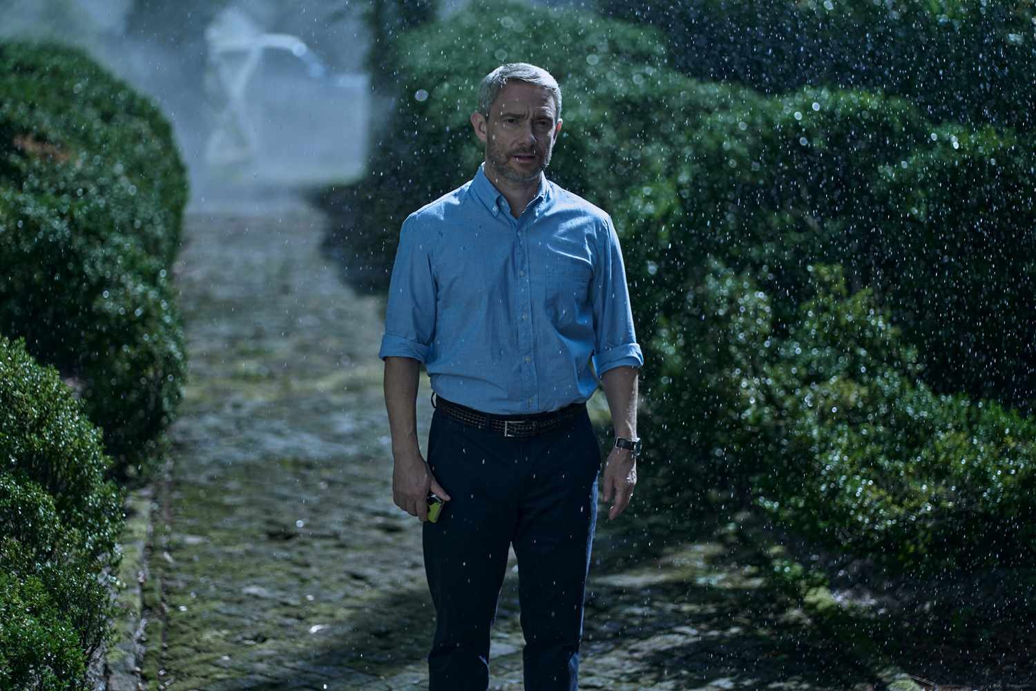 Martin Freeman stand in the rain in the middle of a garden in Miller's Girl