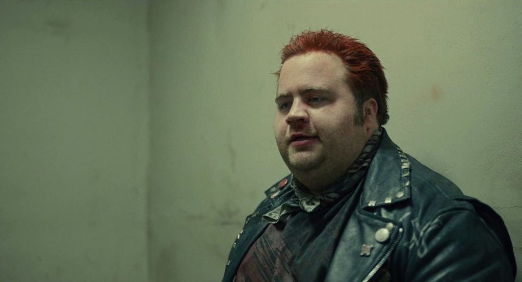 Paul Walter Hauser has a conversation in an empty room in a still from Cruella