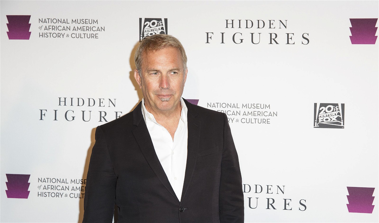 Kevin Costner smiling on the red carpet for a screening of the film Hidden Figures