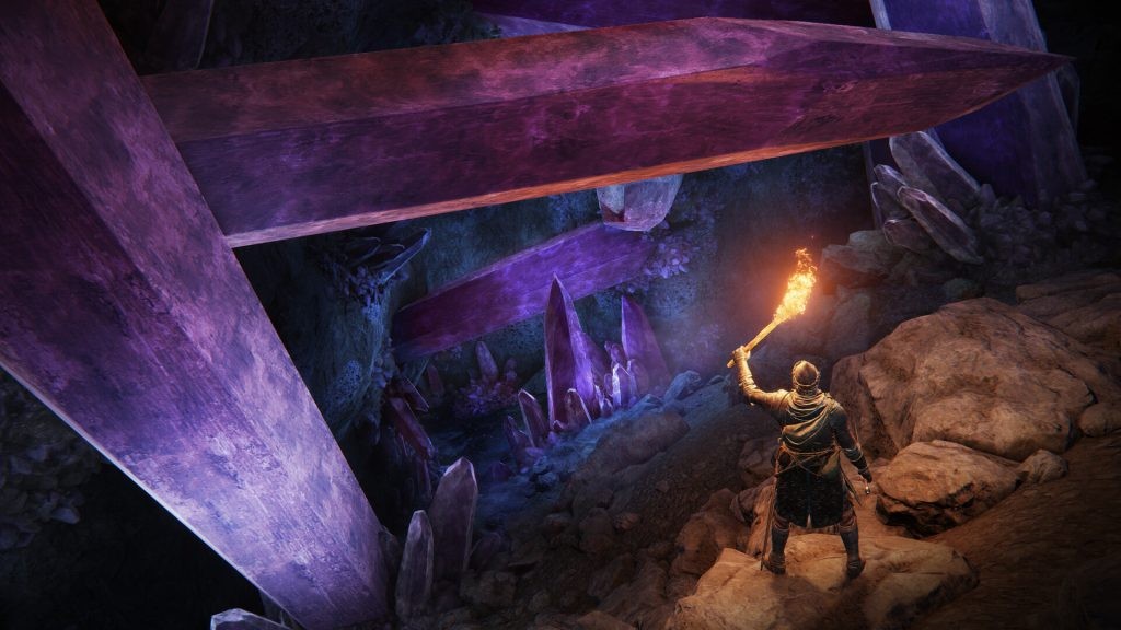 A Tarnished from Elden Ring looking down into a crystal cave while holding a flaming torch above their head.