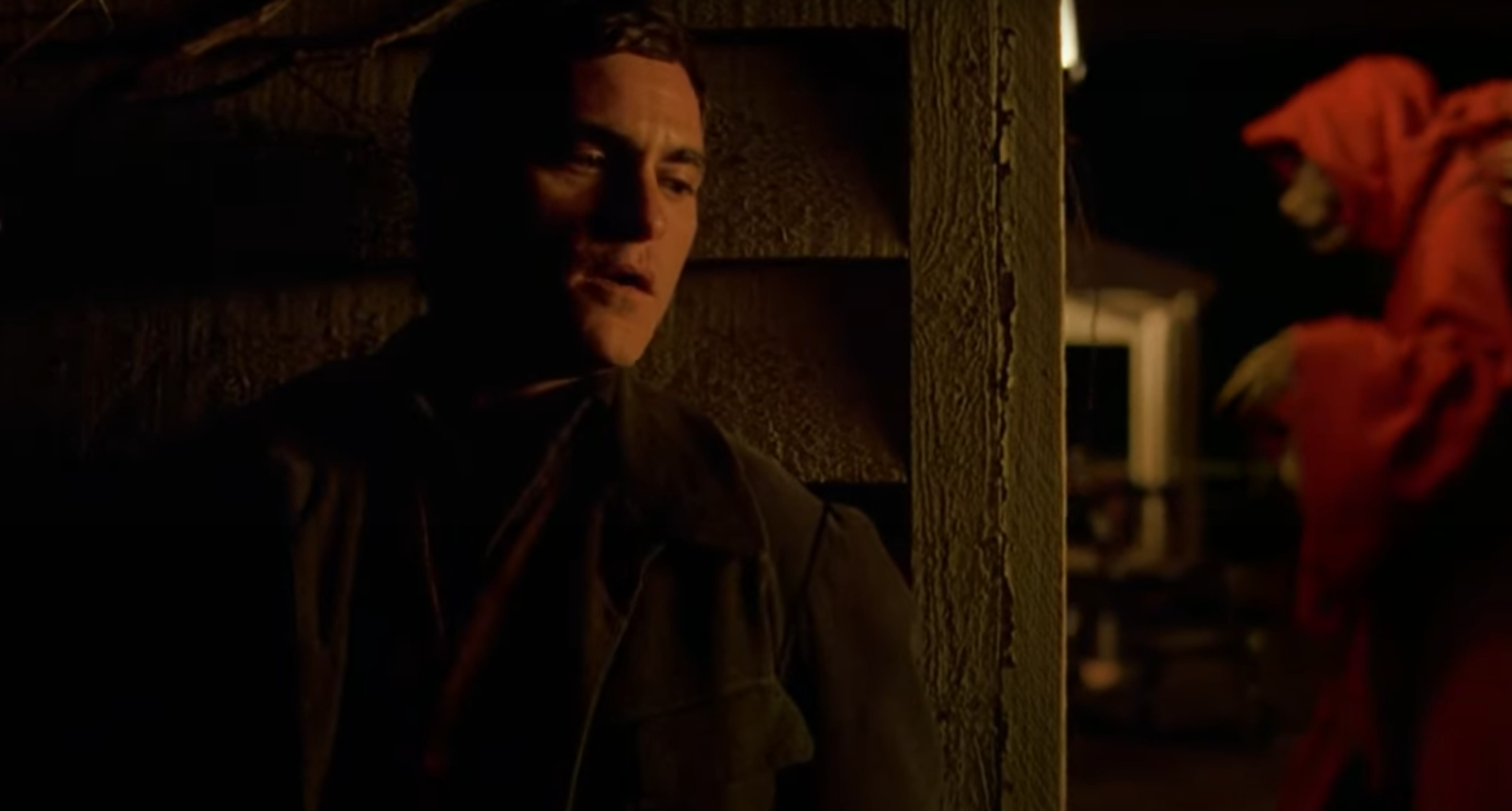 Joaquin Phoenix stands with his back against the wall and seems to be hiding from something in the movie “The Village”