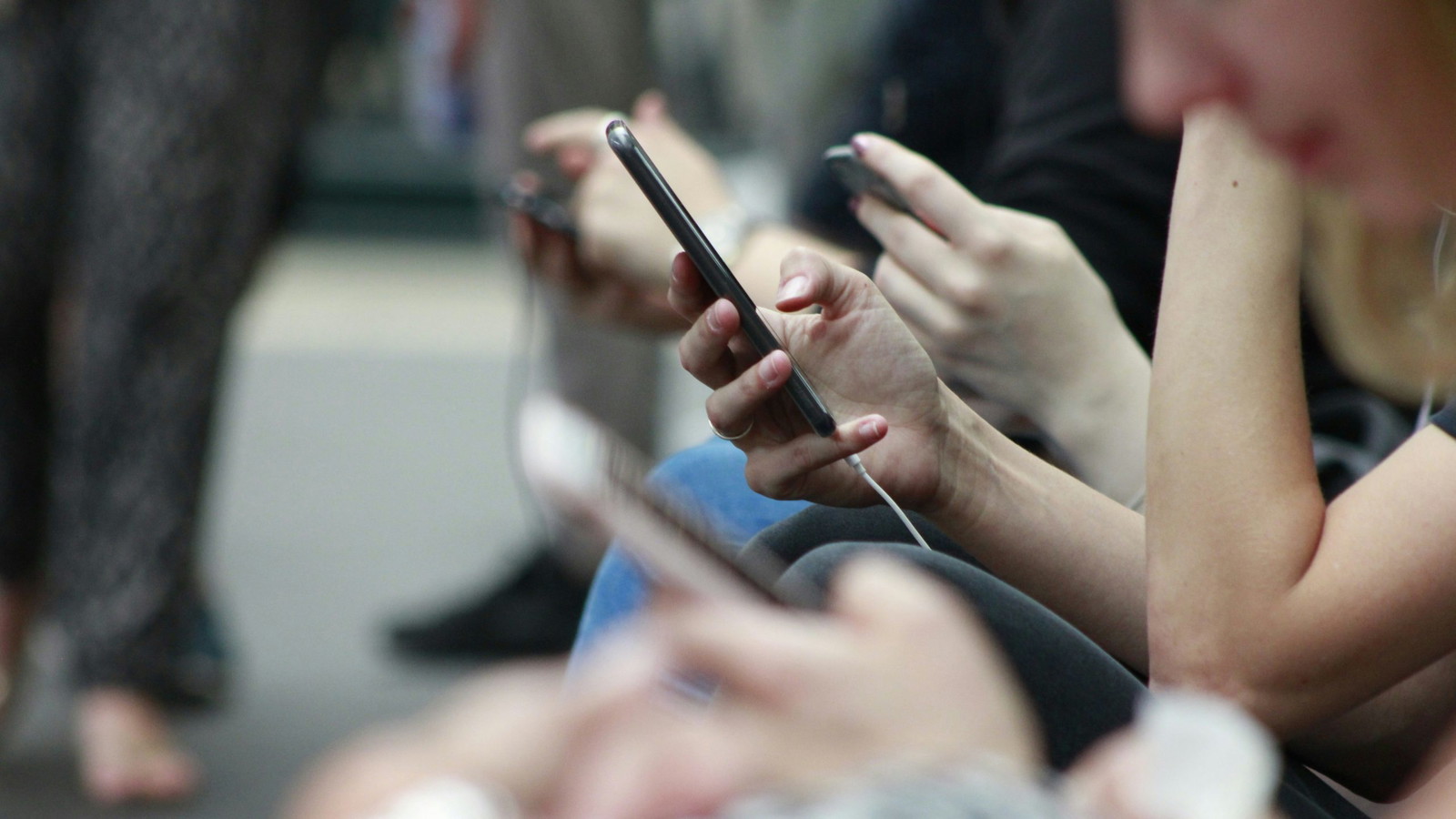 A crowd of people holding up their phones and using them with one being focused on.