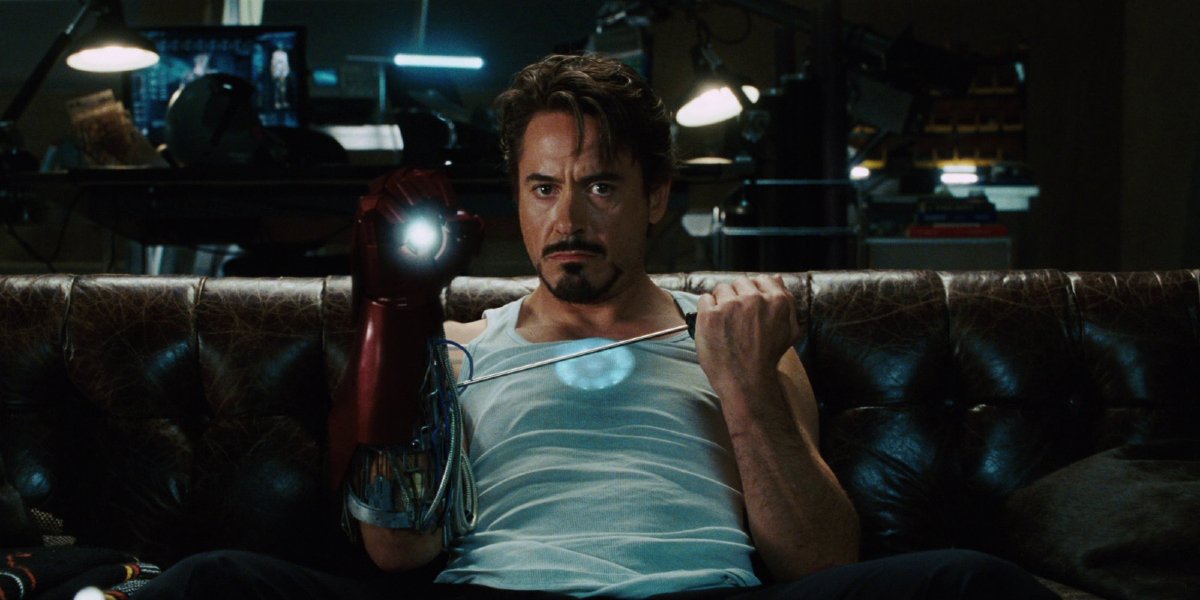 Robert Downey Jr. as Tony Stark in Ironman sitting on a couch and fixing his gauntlet.