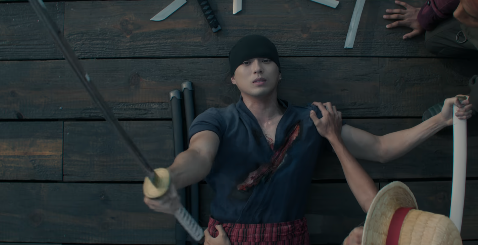 Mackenyu as Zoro is laying on the ground with a wound on his chest in One Piece Live-Action