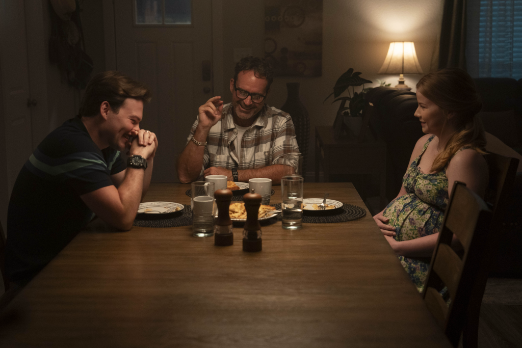 The family is having dinner in Armor. Josh Wiggins laughs at a joke from his character's father, played by Jason Patric. Lanie Stibing plays Josh Wiggins' wife, and her character is pregnant. She laughs from the other side of the table. 