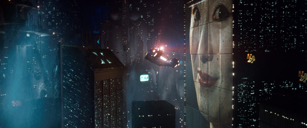 Ridley Scott directs Blade Runner. A giant face lights up the LA skyline as an ad featuring a woman plays. 