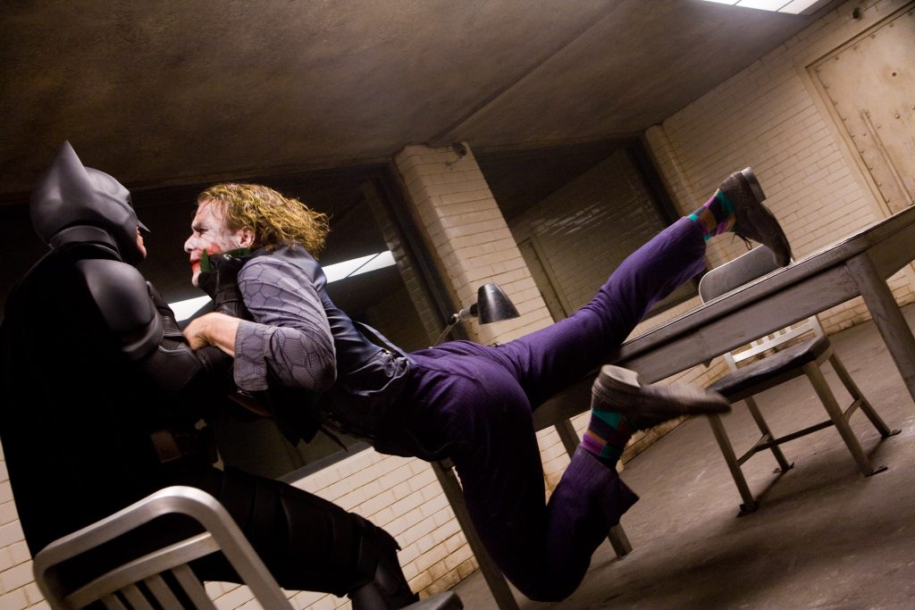Batman picking up Joker by the cuff in an interrogation room as the camera tilts in Christopher Nolan's The Dark Knight.