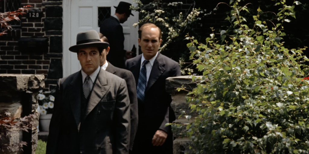 Al Pacino as Michael Corleone, walking in a black suit and hat. 