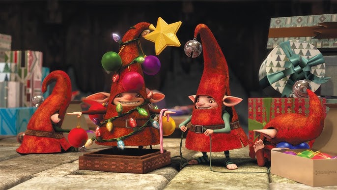 An animated scene from 'Rise of the Guardians' showing several of North's elves in their distinctive red pointed hats with bells. The elves are gathered around a string of colorful Christmas lights, with one elf tangled in them and another holding a golden star ornament.