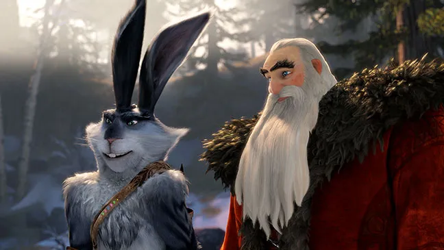 A close-up shot of the Easter Bunny and North (Santa Claus) from 'Rise of the Guardians'. They appear to be outdoors in a snowy, forested area with sunlight filtering through the trees in the background.