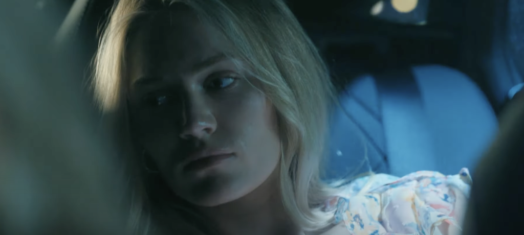 Michelle Randolph as Asinsley, sitting in a car. 