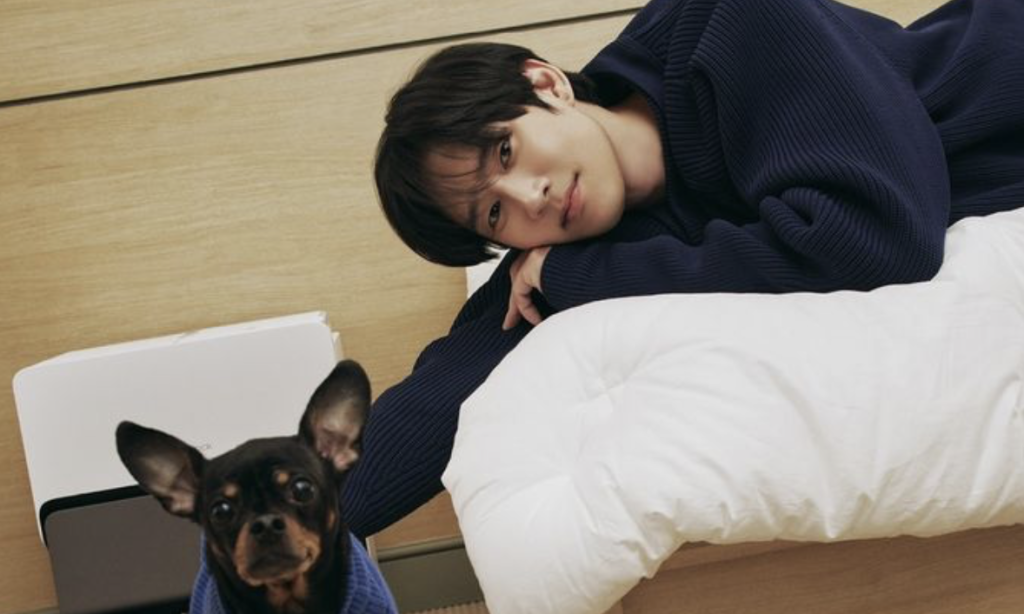 Park Sung Hoon lying on the bed in a dark blue sweater and petting his dog. 