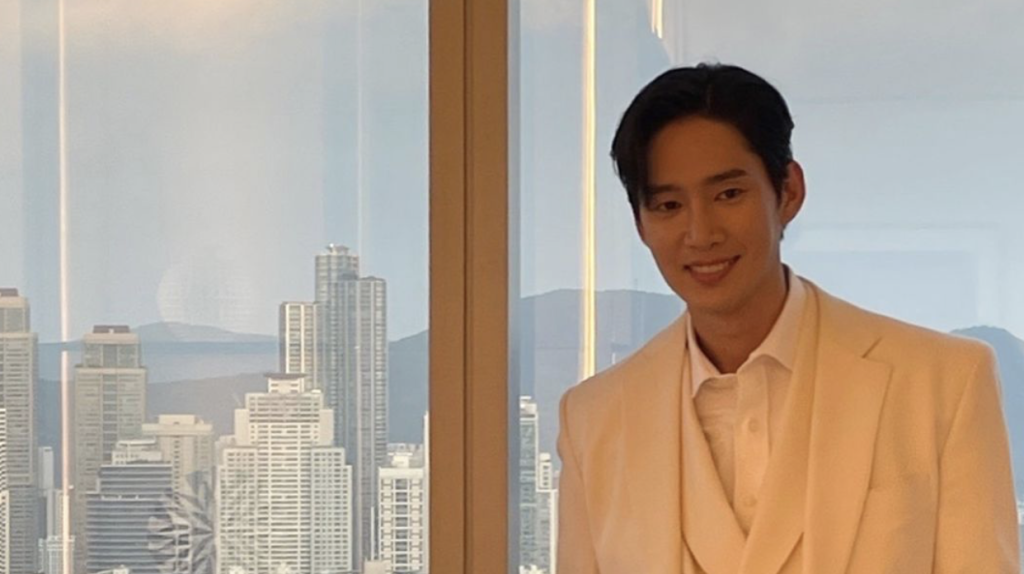 Park Sung Hoon wearing a white suit and posing in front of a glass window. 