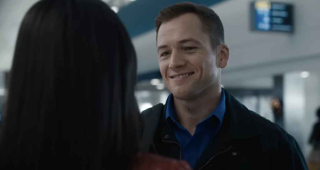 Taron Egerton smiling and weating a black jacket in Carry On