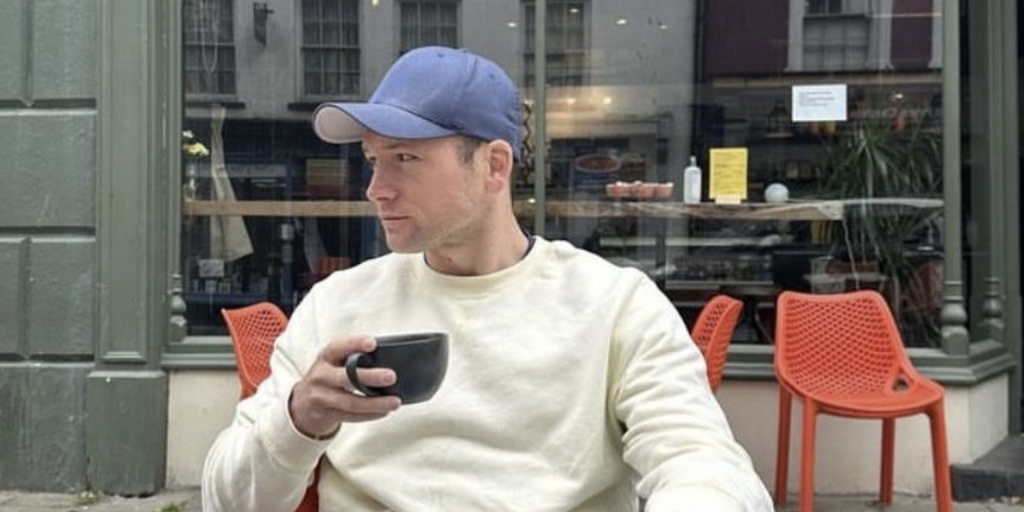 Taron Egerton holding a cup and sitting at an outdoor cafe