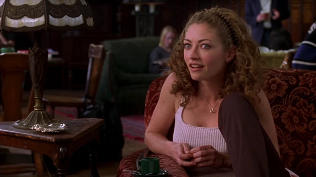 Rebecca Gayheart as Nurse Brenda Bates in a still from the 1998 movie "Urban Legend." She is sitting on a couch conversing with someone off-camera.