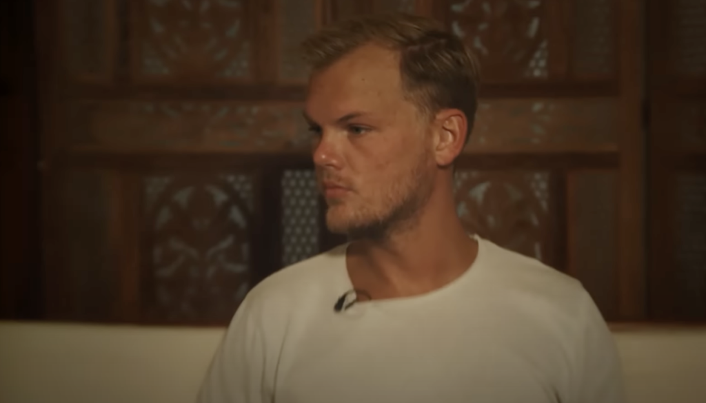 Avicii wearing a white T-shirt and sitting on a white sofa