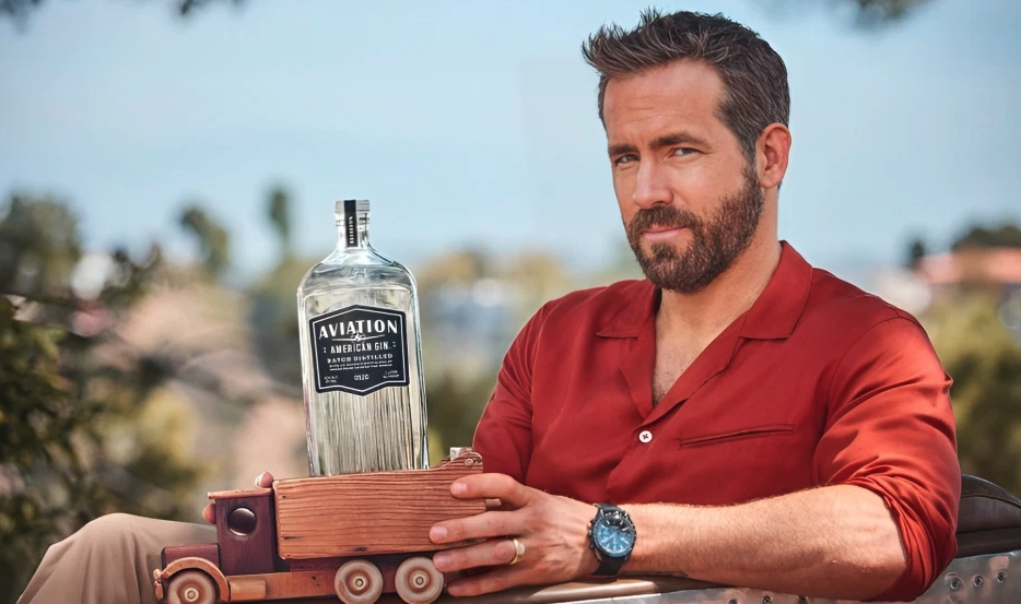 Ryan Reynolds poses with a bottle of Aviation Gin that is kept in a mini wooden truck 