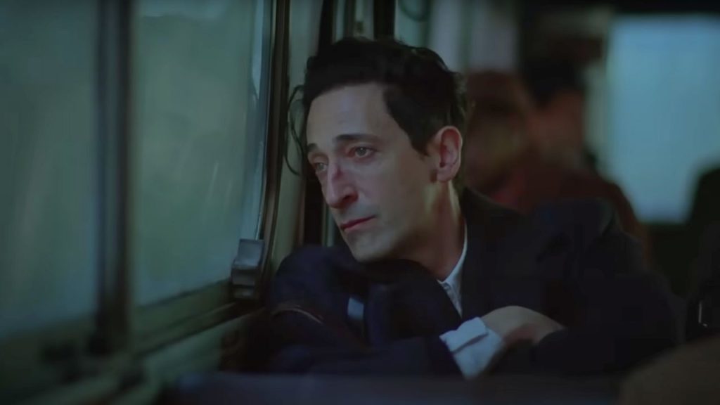 Adrien Brody looking sad, reflecting on his life in The Brutalist