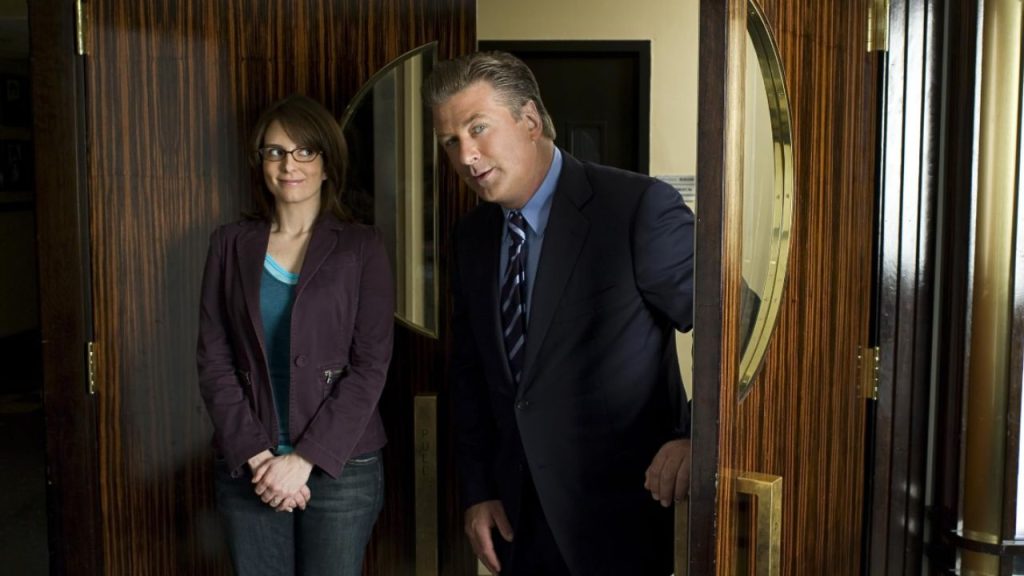 Tina Fey making a funny expression as Alec Baldwin enters a room in 30 Rock