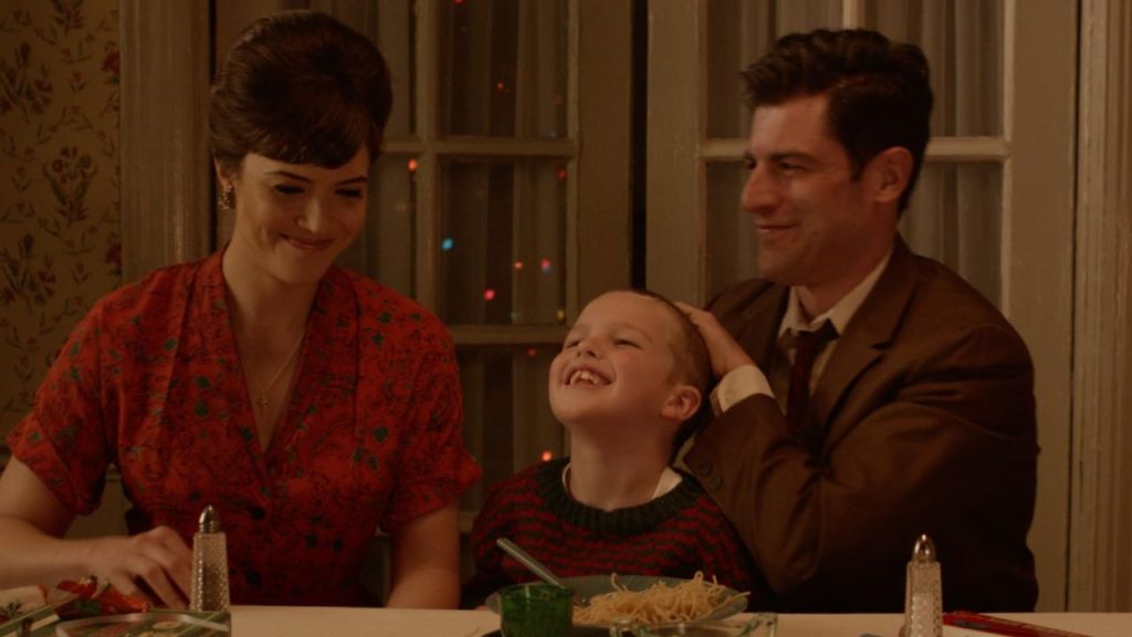 Max Greenfield, Mandy Moore, and Iain Armitage sitting together during a party in I'm Not Here