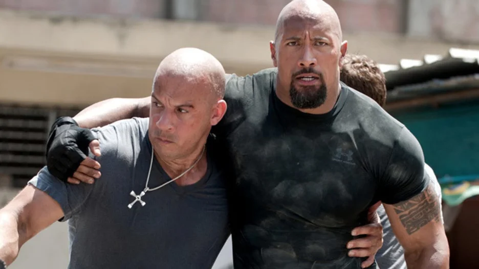 An action scene from Fast & Furious 6 showing Vin Diesel as Dominic "Dom" Toretto and Dwayne "The Rock" Johnson as Luke Hobbs holding and supporting each other.