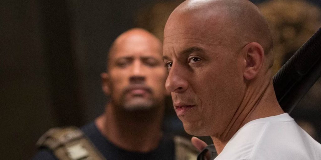 A close-up shot  from Fast & Furious 6 showing Vin Diesel as Dominic "Dom" Toretto and Dwayne "The Rock" Johnson as Luke Hobbs. Dom in the foreground looking stern and Hobbs slightly blurred in the background.