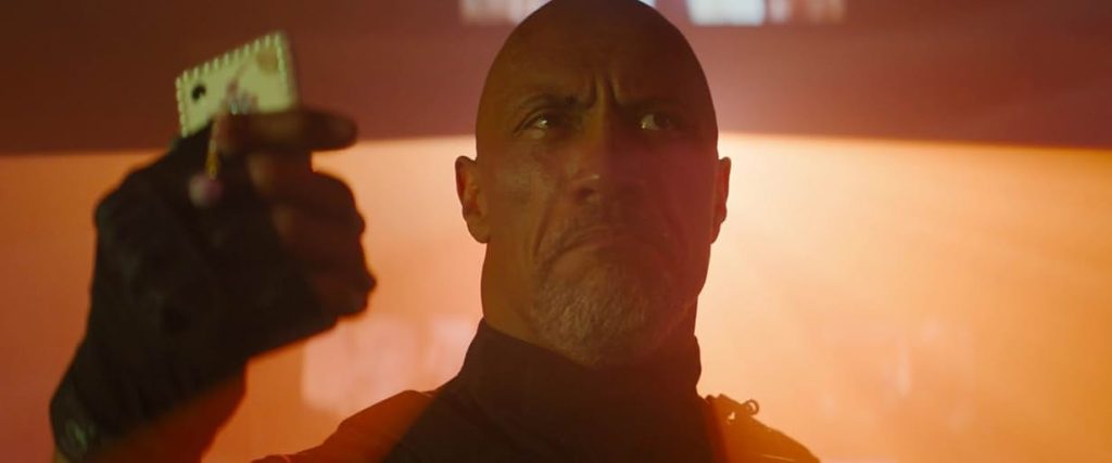 A dramatic close-up shot of Dwayne "The Rock" Johnson as Luke Hobbs in a scene from Fast X. His expression is stern and determined.