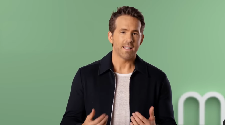 The Canadian actor Ryan Reynolds in a dark jacket against a green background.