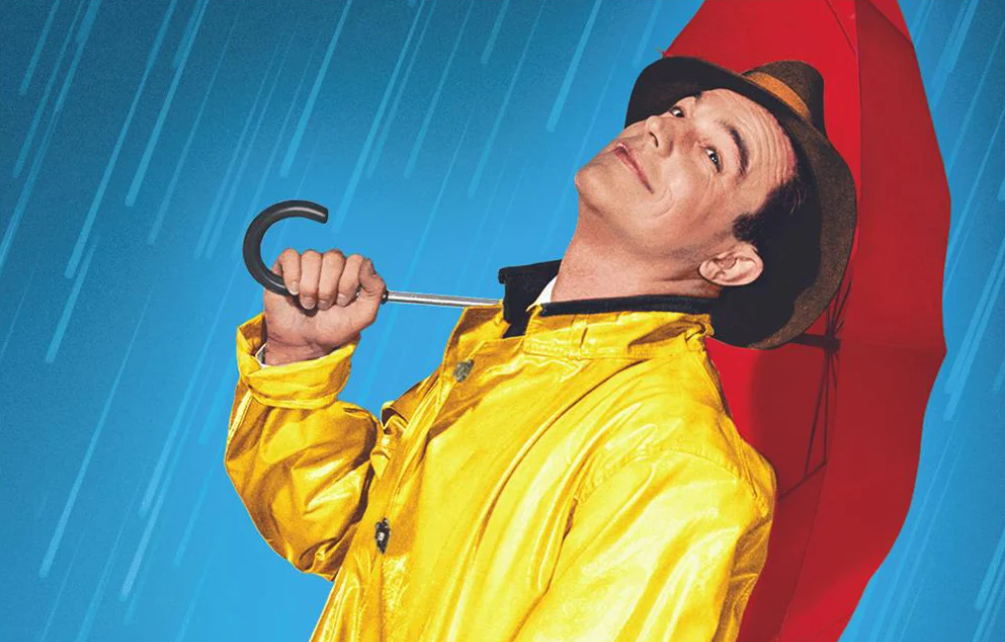 Gene Kelly as Don Lockwood in the musical romantic comedy movie Singin’ in the Rain wearing a yellow raincoat and with a red umbrella in his hand.