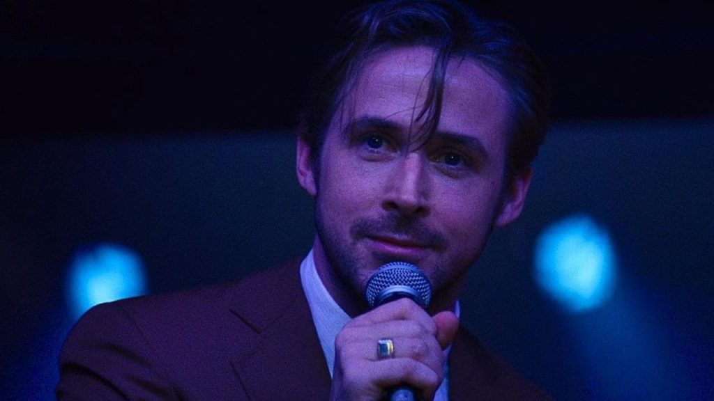 Ryan Gosling as Sebastian Wilder in La La Land wearing a suit and holding a microphone.