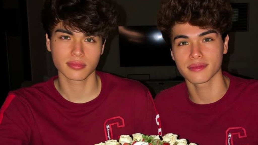 The Stokes Twins wearing identical red t-shirts with a cake in front of them.