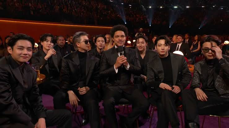 Trevor Noah hosting the 2022 Grammy Awards while being seated with the BTS