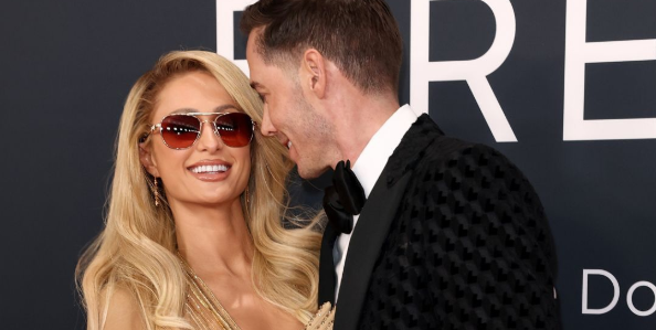 Paris Hilton in red sunglasses with her husband Carter Reum wearing a black suit at Grammy 2025.