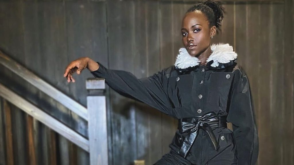 Lupita Nyong’o standing beside a staircase posing for a picture