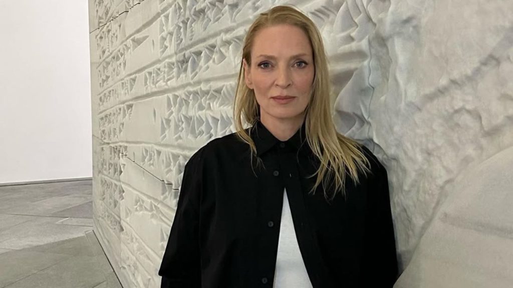 Uma Thurman standing beside a decorated wall