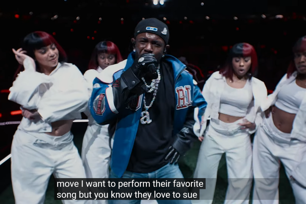 Kendrick Lamar holding a mic surrounded my performers in white dress. 