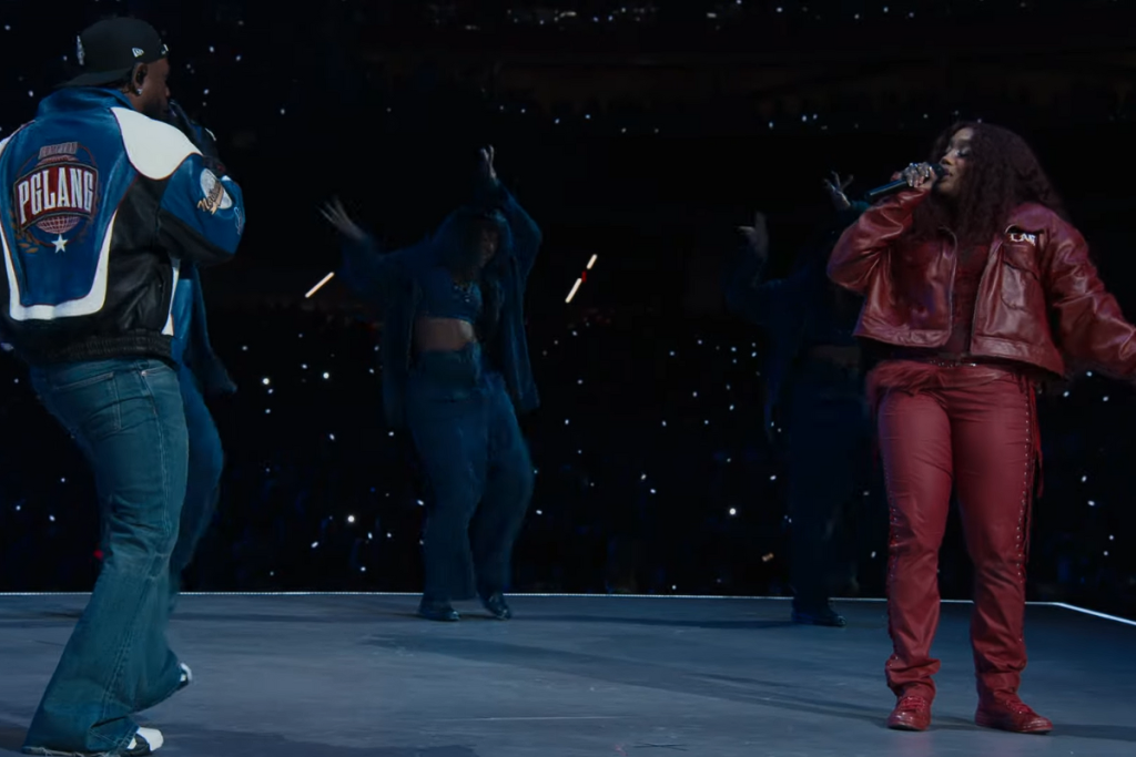 Kendrick Lamar wearing a blue cap, jacket, and jeans performing Luther with SZA wearing a red jacket and pants. 