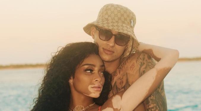 Winnie Harlow and Kyle Kuzma posing together on a beach, dressed casually in beachwear. 