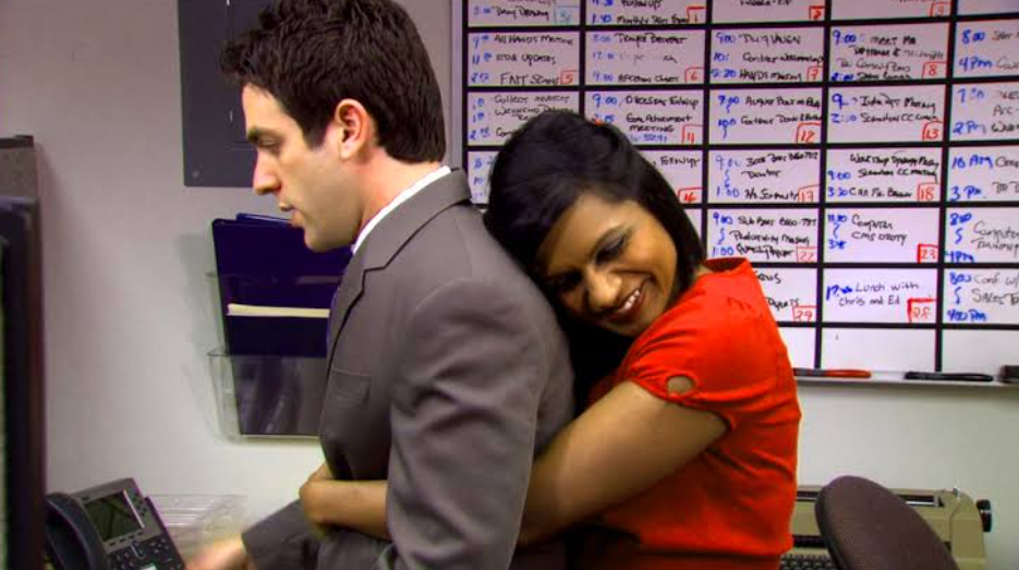 Kelly Kapoor playfully hugging Ryan Howard from behind in a lighthearted moment from The Office.