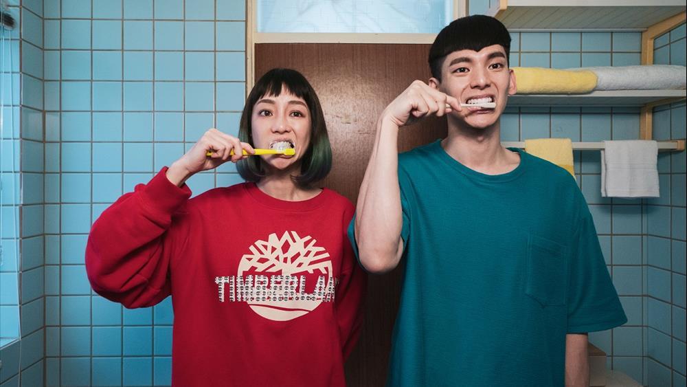 Nikki Hsieh and Austin Lin in 'I WeirDo' are brushing their teeth in a bathroom with blue tiled walls.